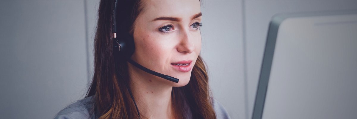 Kontakt Header  Eine Frau mit dunklen Haaren und Headset welche am sprechen ist